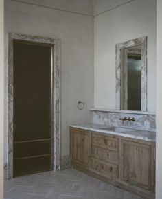 an empty bathroom with marble counter tops and wooden cabinetry, along with two mirrors on the wall