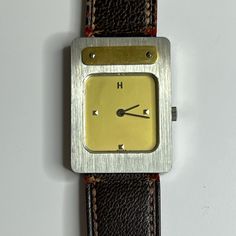 Herms Stainless Steel And Gold Plated Manual Wind Watch. Bezel - Stainless Steel With Vertical Brushed Finish. Rectangular Gold Colored Plate With Two Screws At Top Of Bezel. Dial - Champagne Gold Color, H At 12:00, Pyramid Shaped Markers At 3,6 And 9:00. Face Measures 16 X 15 Mm. Case - Measures 29 X 21 Mm. Case Back Stamped With Hermes And 1751. Strap - Brown Fine Grained Leather On Exterior And Gold Smooth Leather On Interior. Stamped M And Bracelet Hermes. 16mm Lug Width- Strap Attachment. L Vintage Leather Watch With Diamond Hour Markers, Silver Leather Watch For Evening, Silver Leather Evening Watch, Bracelet Hermes, Champagne Gold Color, Hermes Accessories, Champagne Gold, Leather Band, Smooth Leather