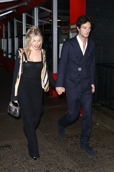 a man and woman are walking down the street holding hands, both wearing black outfits