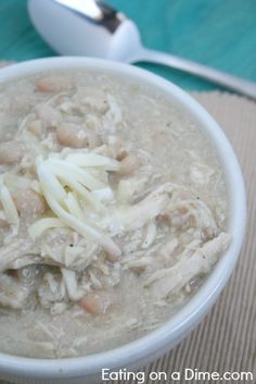 a white bowl filled with chicken and noodles next to a spoon on top of a table