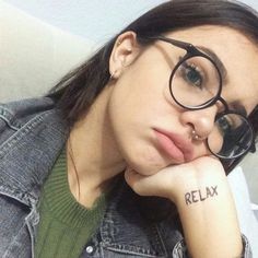 a woman wearing glasses with the word relax written on her arm behind her head, looking at the camera