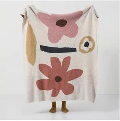 a white blanket with pink and brown flowers on it, sitting in front of a white wall