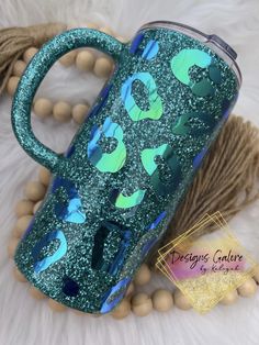 a blue and green glittered coffee cup with an animal print on it next to some beads