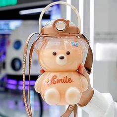 a person holding up a small teddy bear in a bag with the name smile on it