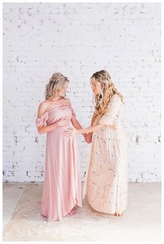 two women standing next to each other in front of a white brick wall holding hands