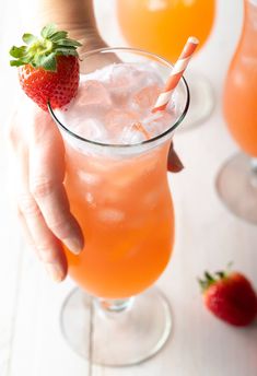 a person holding a drink with strawberries on the rim and two glasses filled with it