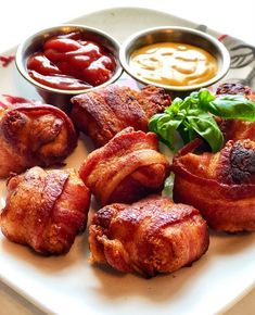 bacon wrapped in bacon and garnished with green leaves on a plate next to dipping sauces