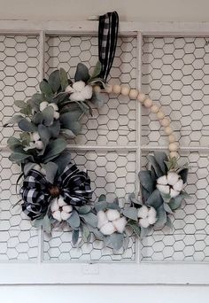 a wreath with cotton balls and eucalyptus leaves is hung on the wall in front of a window