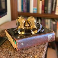 two binoculars sitting on top of an old book in front of a bookshelf