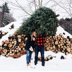 two people standing next to each other in the snow with a tree on their shoulders