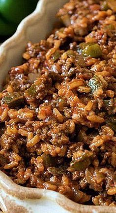 a bowl filled with rice and vegetables on top of a wooden table next to green peppers