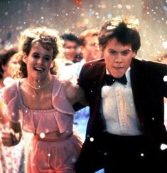 two people dressed in formal clothes and tuxedos are dancing with confetti falling from the sky