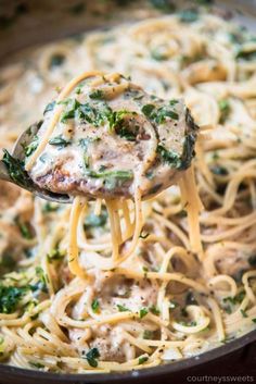 a spoon full of pasta with meat and spinach on it is being lifted from the skillet