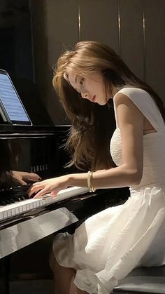 a woman in a white dress playing a piano with her hands on the keyboard and looking down