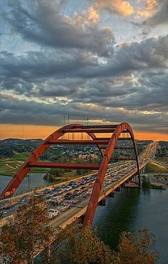 a red bridge over a river with cars driving on it and the sun going down