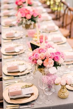 a long table is set with pink flowers and gold place settings for an elegant dinner