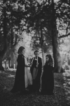 three women standing in the woods talking to each other and one woman is wearing a long black dress