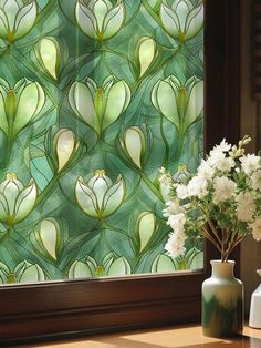 a vase with white flowers sitting next to a window covered in green and yellow stained glass