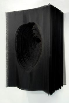 an open book with black paper on it's cover is hanging from the wall