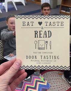 a person holding up a sign that reads eat, taste and read with children in the background