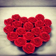 a heart shaped box filled with cupcakes covered in red frosting roses on top of a table