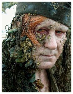 a close up of a person with mud on his face and hair covered in plants