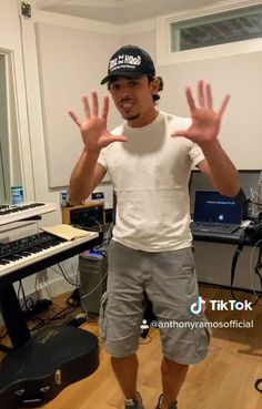 a man standing in front of a keyboard with his hands up and wearing a hat