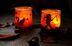 two glass jars filled with candles sitting on top of a wooden table next to leaves