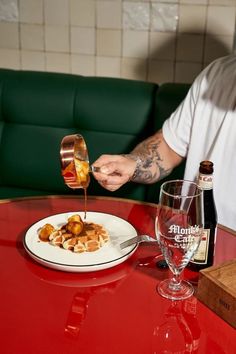 the man is pouring sauce on his plate with food and wine in front of him