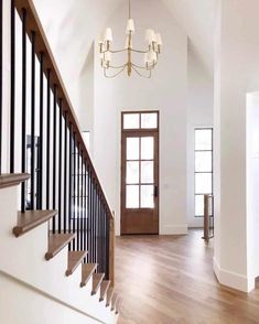 an empty foyer with wood floors and white walls, chandelier above the stairs