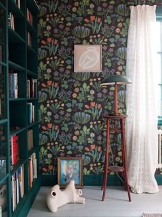 a room with green bookshelves and wallpaper on the walls, along with a white floor lamp