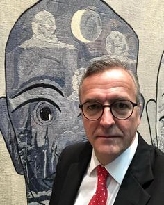 a man wearing glasses and a red tie standing in front of a wall with an image of a human head on it