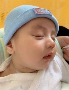 a baby wearing a blue hat laying on top of it's head with its eyes closed