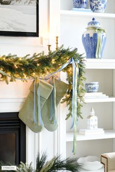 stockings hanging from the mantle in front of a fireplace with christmas decorations on it and blue and white vases