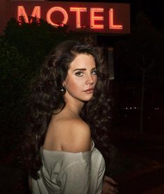 a woman standing in front of a motel sign at night with her hair blowing in the wind