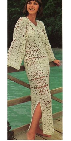 a woman standing on a wooden bridge next to the water wearing a white crocheted dress