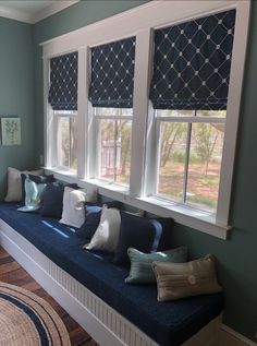 a blue window seat with pillows on it in front of three windows that have matching shades