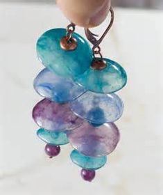 a pair of earrings is hanging from a hook on a marble counter top with purple and blue beads