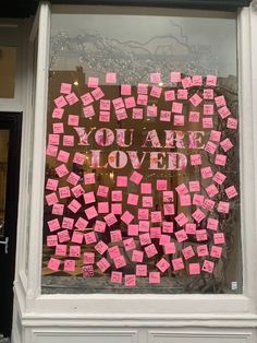 a store window with pink sticky notes written on the glass and writing you are loved