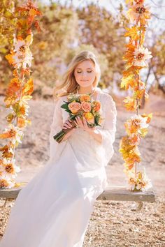 a woman in a white dress sitting on a swing with flowers and greenery around her