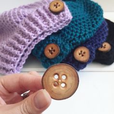 a hand holding a button in front of three knitted hats with buttons on them