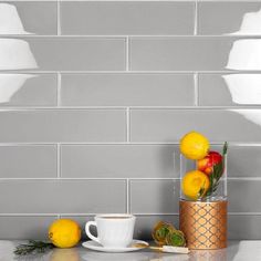 a cup of coffee and some lemons on a white counter with silver tiles behind it