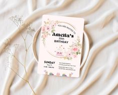 a birthday card sitting on top of a white table cloth next to a flowery plant