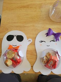 two white ghost shaped plates with candy and candies in them on a wooden table