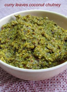 a white bowl filled with green food sitting on top of a cloth covered tablecloth