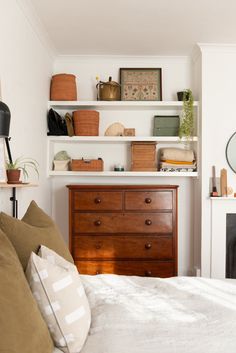 a bedroom with white walls and shelves filled with items on top of the headboard