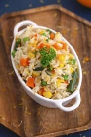 a white bowl filled with rice and veggies on top of a wooden cutting board