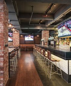 an empty bar with chairs and televisions in the back ground, along with brick walls