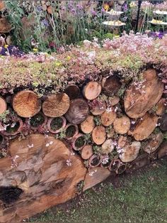 a large pile of wood sitting on top of a grass covered field next to flowers