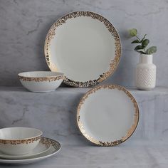 white and gold dinnerware set on marble countertop with flowers in vase behind it